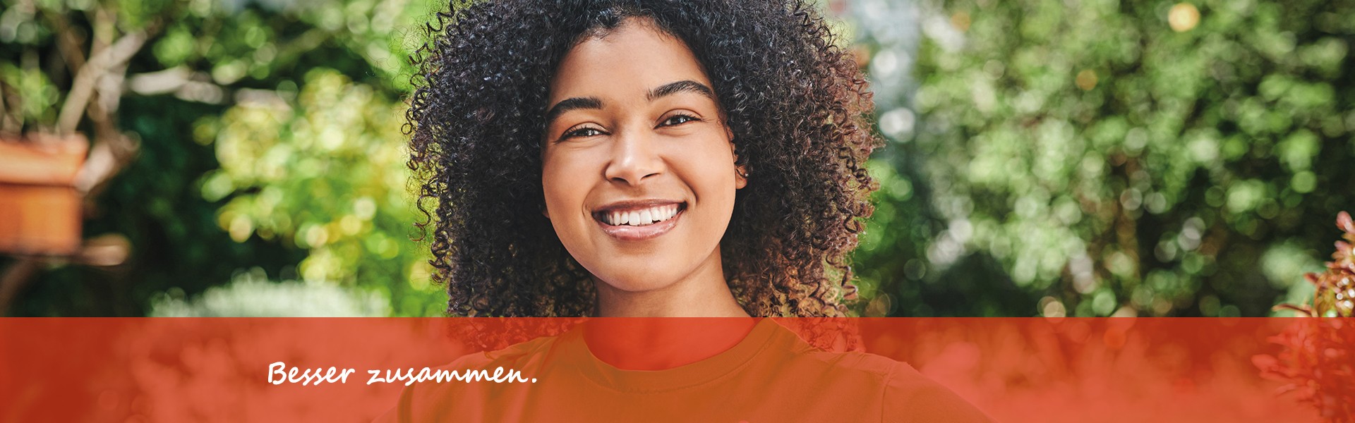 Lächelnde Frau mit lockigem Haar in grünem T-Shirt vor grünem Gartenhintergrund