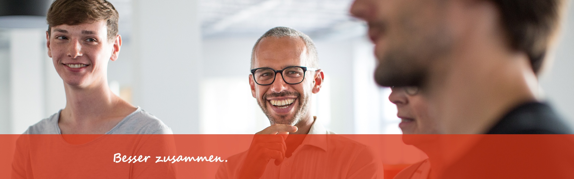 4 Personen stehen in einem Büro und besprechen sich, zwei Männer lächeln